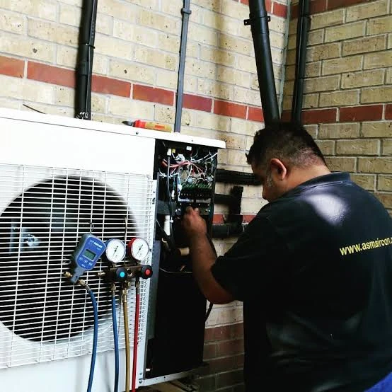 Technician checking an HVAC unit with pressure gauges beside a brick wall